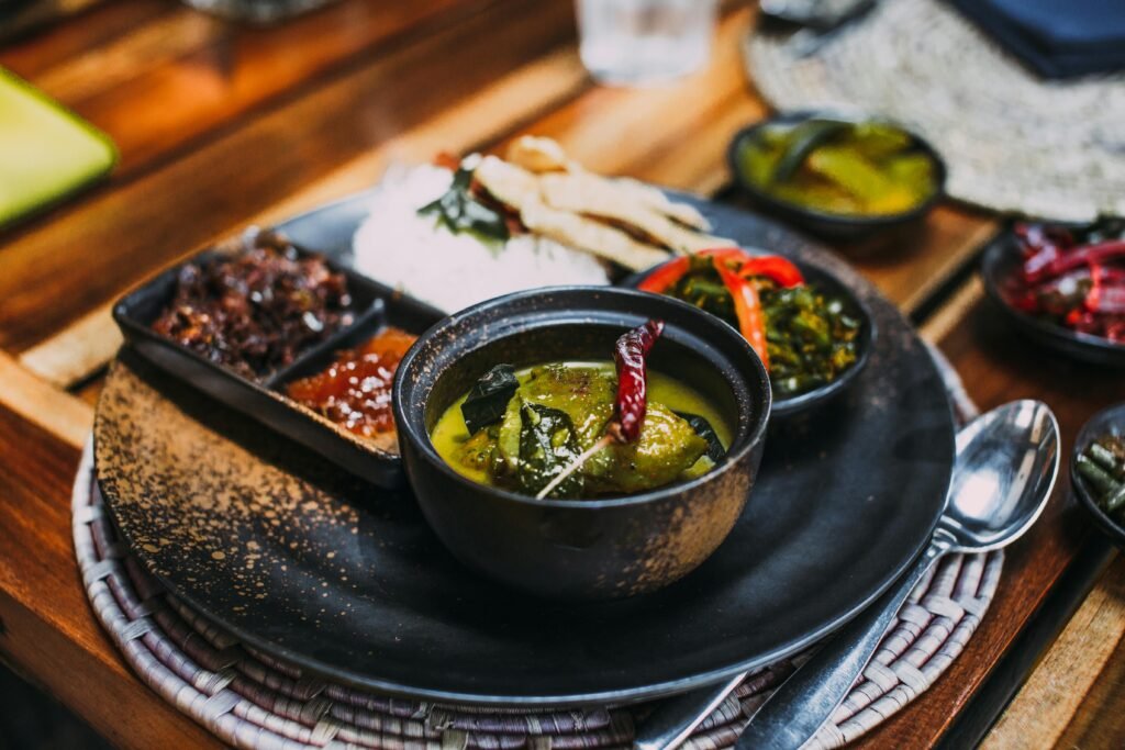 Close-up of a delicious Asian dish featuring curry, chili peppers, and side dishes served in a black bowl.
